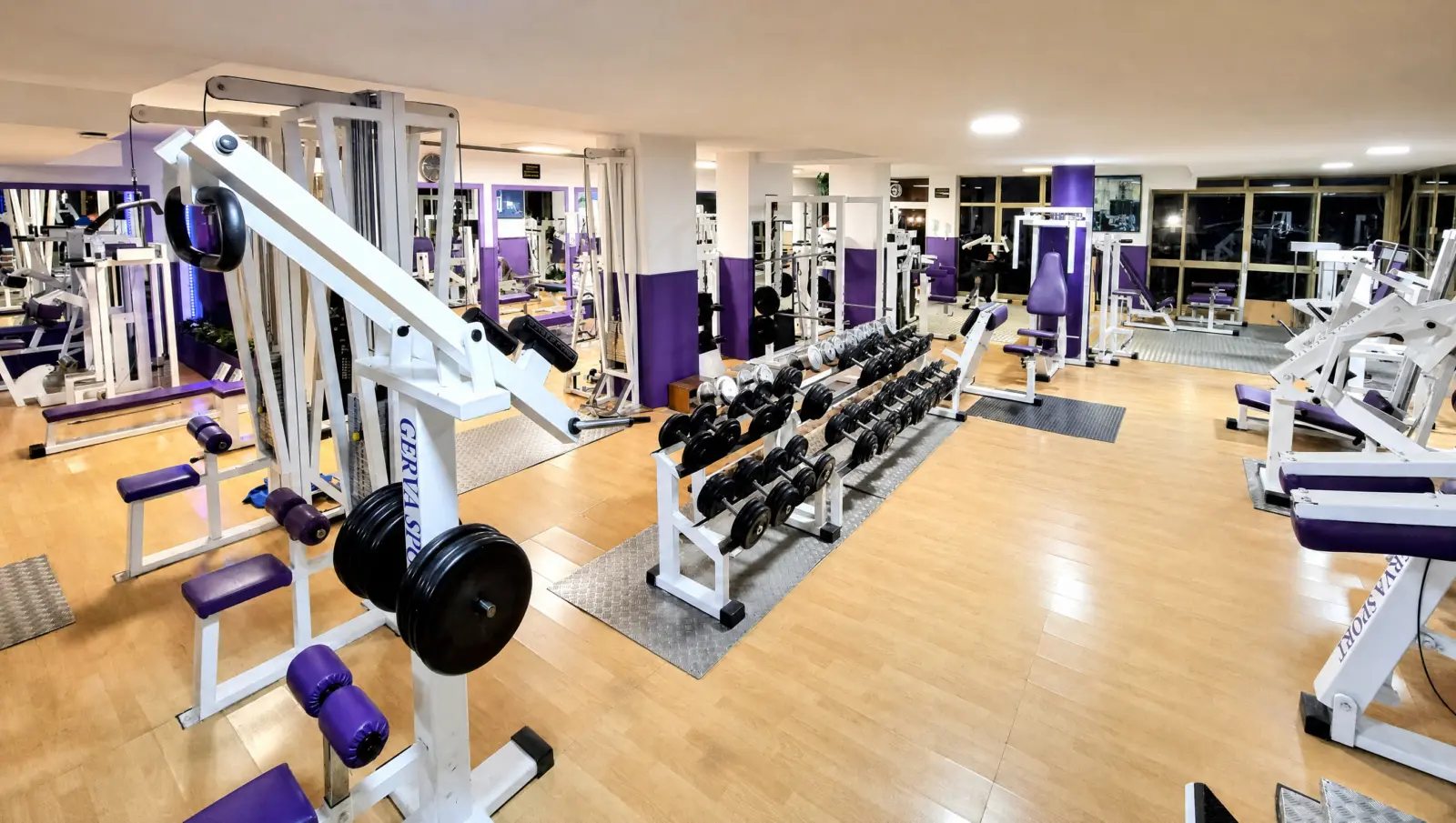 Sala de musculación de Athena con máquinas blancas y tapicería morada, recreación de una fotografía del gimnasio